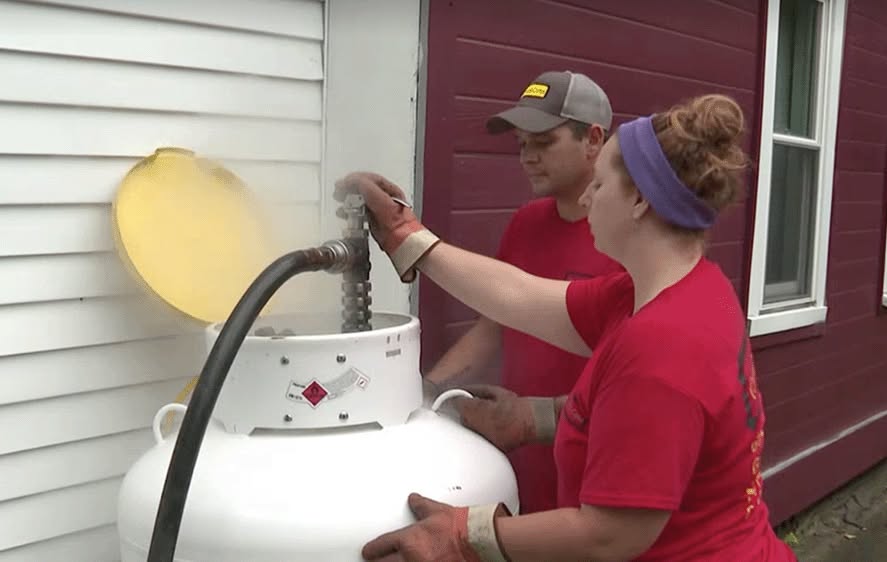 close up of two people filling a propane tank beside a white house
