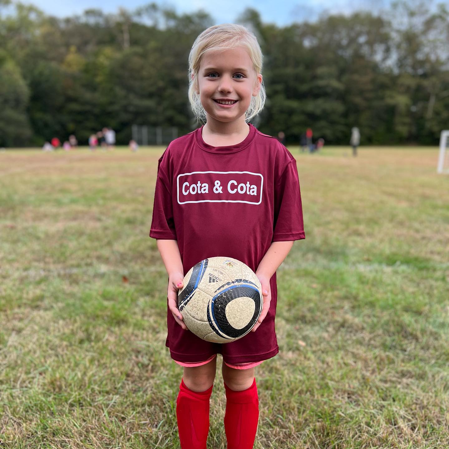 A girl wearing a red tee shirt reading 'Cota & Cota' holding a soccer ball. 